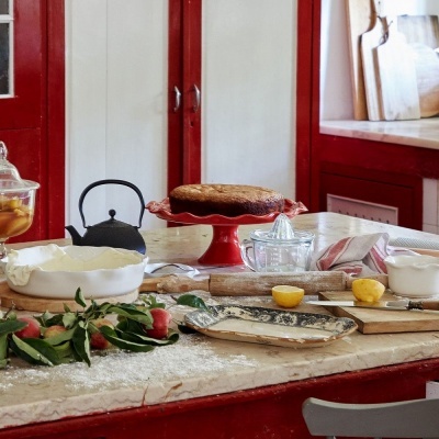 Bancada de cozinha vermelha com tarte, chaleira, jarro, limões e utensílios de cozinha