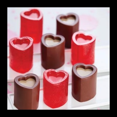 Chocolates em forma de coração com coberturas vermelha e castanha sobre fundo branco e rosa