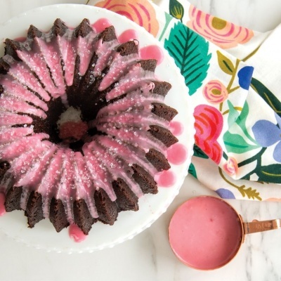 Bolo de chocolate com cobertura rosa em prato branco e panela com molho rosa ao lado