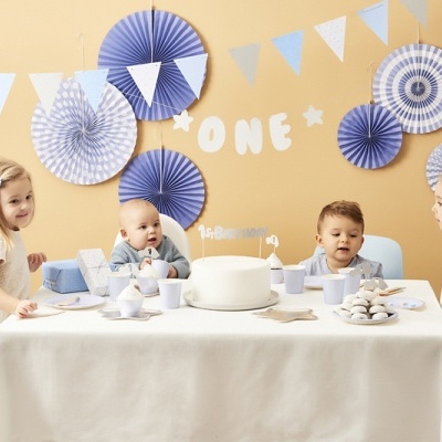 Crianças à mesa com bolo branco e decoração azul e branca numa festa infantil