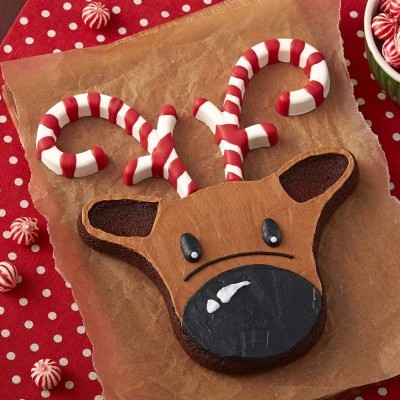 Bolo em forma de rena com cornos em padrão vermelho e branco tipo candy cane sobre pano vermelho com bolinhas brancas