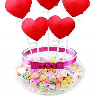 Taça de vidro com doces coloridos em forma de coração e pirulitos vermelhos em forma de coração no topo