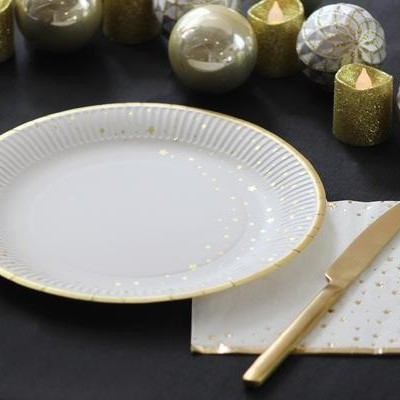 Conjunto de prato branco com detalhes dourados e talheres dourados numa mesa decorada