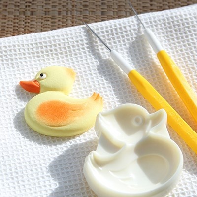 Patinho amarelo, forma de silicone e ferramentas amarelas sobre toalha branca