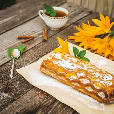 Pastelaria retangular dourada com açúcar em pó, flores amarelas e chá numa mesa de madeira