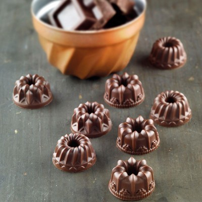 Bombons de chocolate em formato de mini bolo sobre superfície cinzenta com recipiente laranja ao fundo