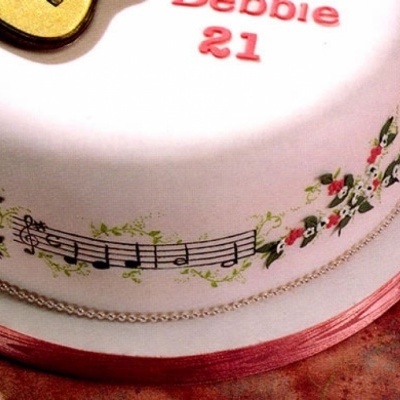 Bolo decorado com notas musicais e flores, texto Debbie 21 no topo