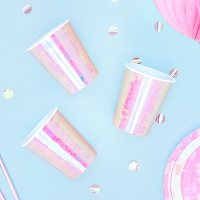 Copos descartáveis iridescentes rosa e dourado com pratos e palhinhas sobre fundo azul