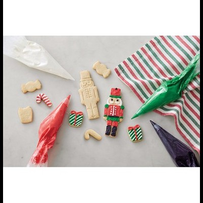 Biscoitos e sacos de confeitar de várias cores para decoração natalícia sobre superfície cinza