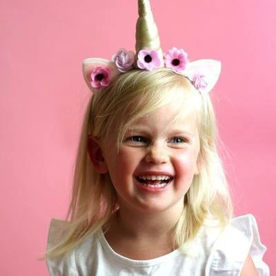 Menina loira com tiara de unicórnio e flores num fundo rosa