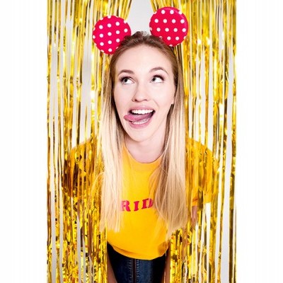 Mulher com t-shirt amarela e faixa de orelhas vermelhas com bolinhas brancas entre cortinas douradas