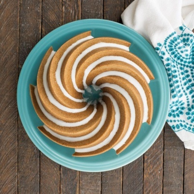 Bolo bundt com cobertura branca num prato azul claro sobre mesa de madeira escura