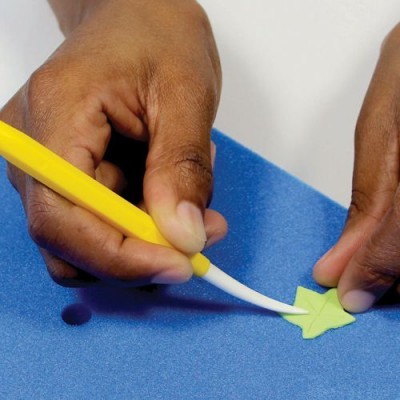 Mãos a cortar forma de estrela verde com estilete amarelo sobre base azul