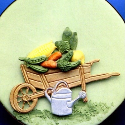 Prato decorativo com relevo mostrando carrinho de mão com legumes e regador.