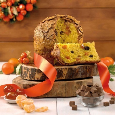 Panetone com frutos secos e cristalizados sobre base de madeira com fita vermelha, tangerinas e cubos de chocolate