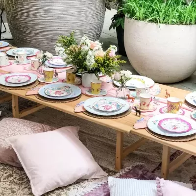 Mesa baixa de madeira com serviço de chá floral e almofadas pastel