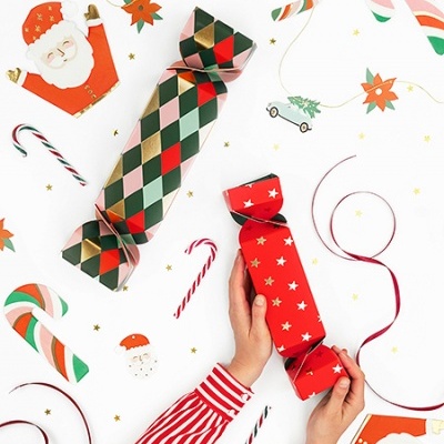 Crackers de Natal com padrões coloridos e decorações festivas ao redor sobre fundo branco.