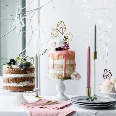 Mesa decorada com dois bolos e cupcakes, velas e decoração minimalista