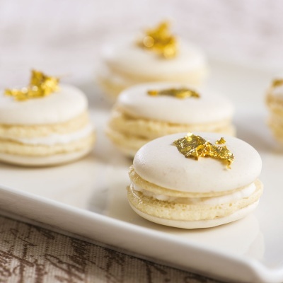 Macarons brancos com decoração dourada sobre travessa branca.