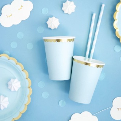 Copos e pratos de papel azul claro com bordas douradas, palhinhas às riscas, merengues brancos e decoração de nuvens em fundo azul.