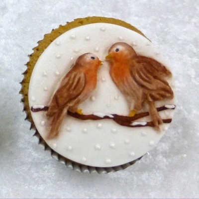 Cupcake com decoração de dois pássaros castanhos sobre galho em cobertura branca