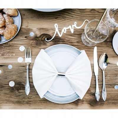 Mesa postada para refeição com prato branco, guardanapo em laço, talheres, copo e decoração com a palavra love.