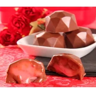 Bombons de chocolate recheados com creme rosa e rosas vermelhas ao fundo