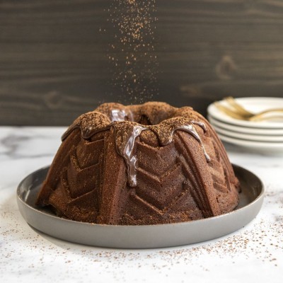 Bolo bundt de chocolate com cobertura e cacau em pó numa mesa com fundo madeira.