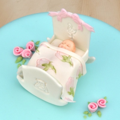 Miniatura bebé adormecido numa cama de baloiço branca com cobertor florido e flores cor-de-rosa