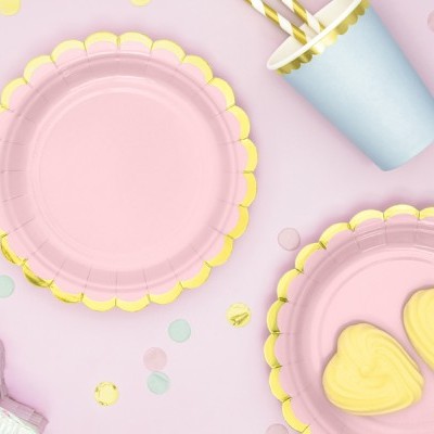 Conjunto de pratos descartáveis cor-de-rosa com borda dourada, copos azuis claros com canudos e biscoitos amarelos em forma de coração