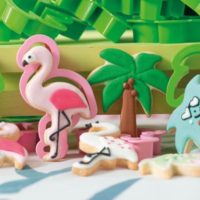 Biscoitos decorados de flamingo e palmeira sobre mesa com forminhas verdes ao fundo