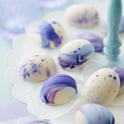 Ovos de chocolate branco com padrões roxos e azuis em prato branco