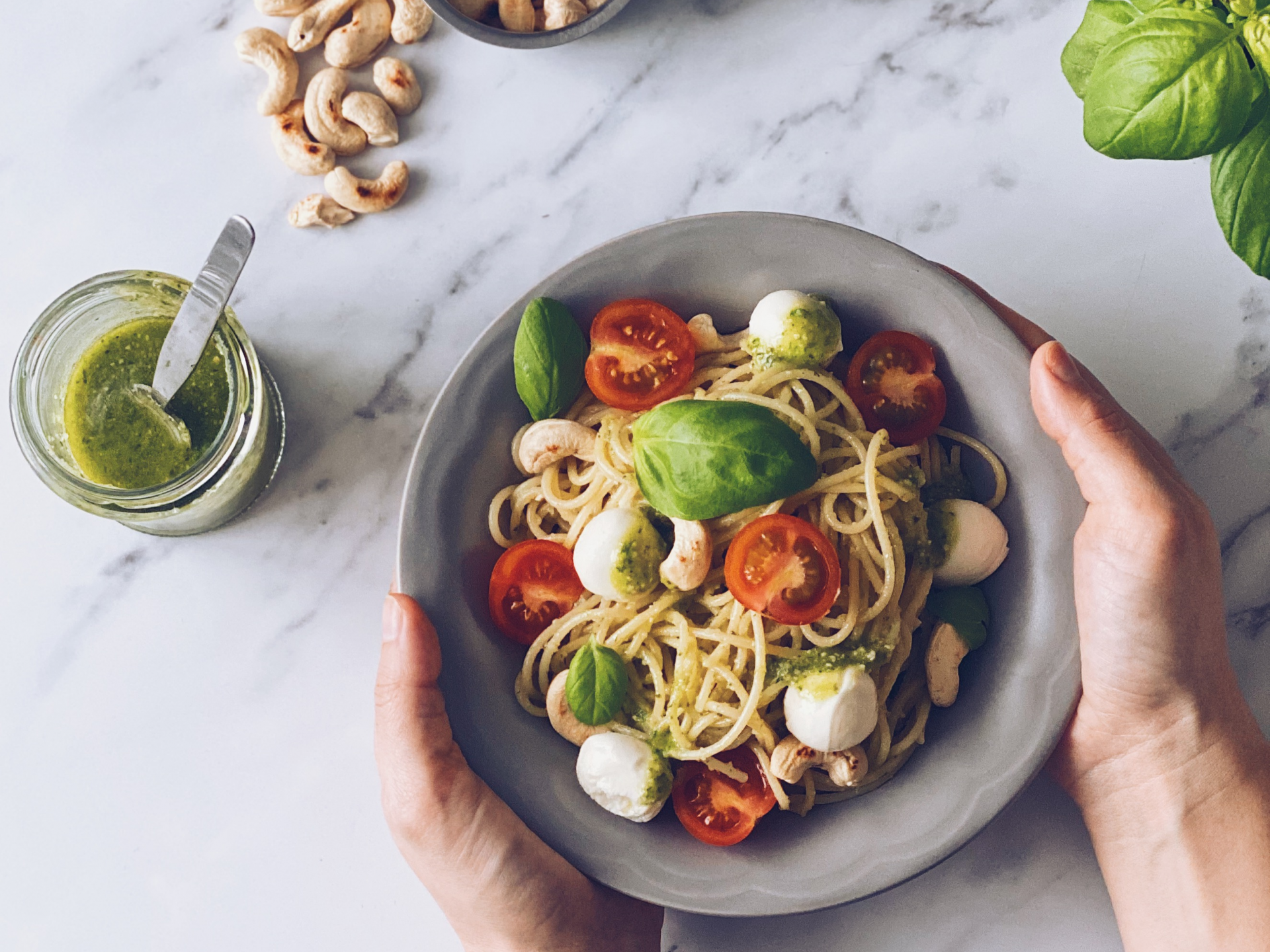 Prato de espaguete com tomate cherry, mozzarella, manjericão e caju com molho verde ao lado