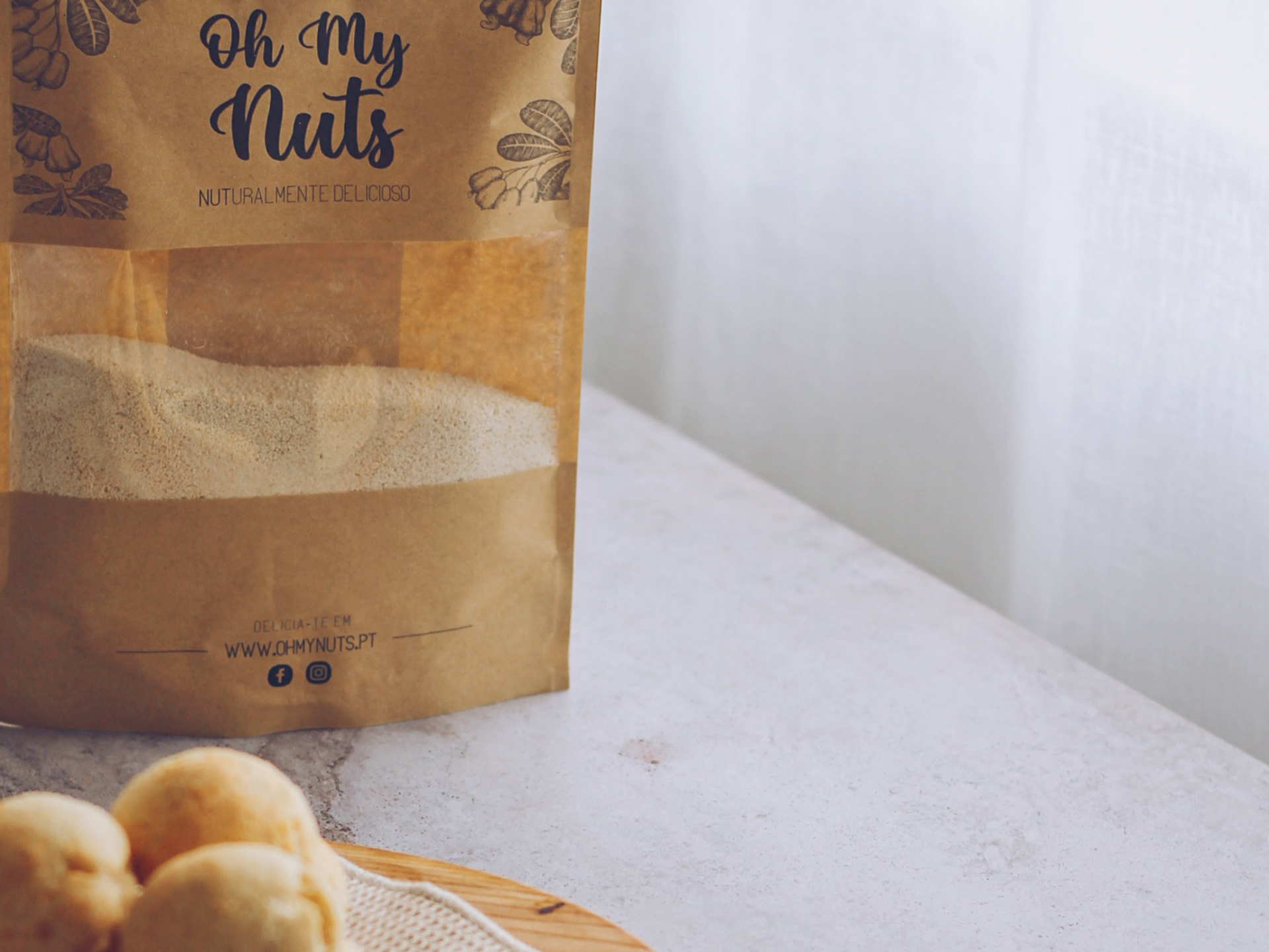 Pacote Oh My Nuts com pó em superfície branca e pão num prato de madeira.