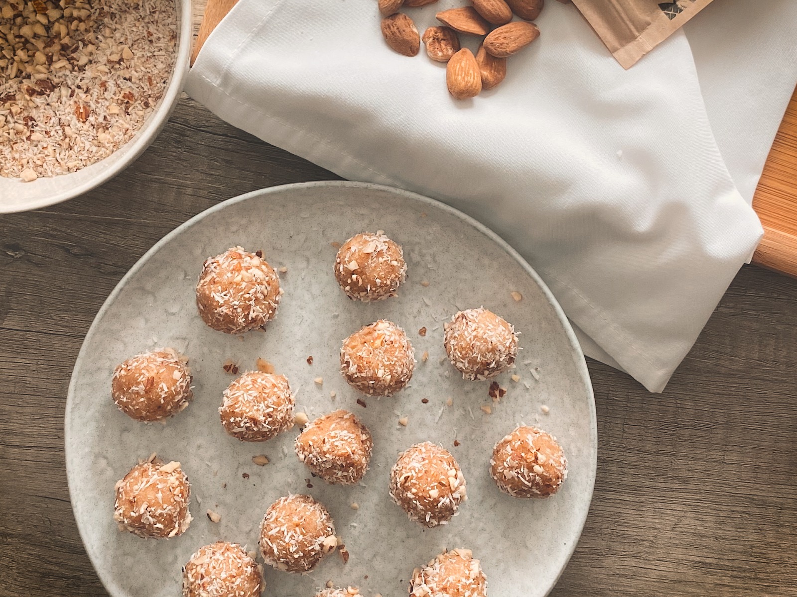 Bolas de energia cobertas de coco numa ânfora cinzenta com ingredientes ao redor