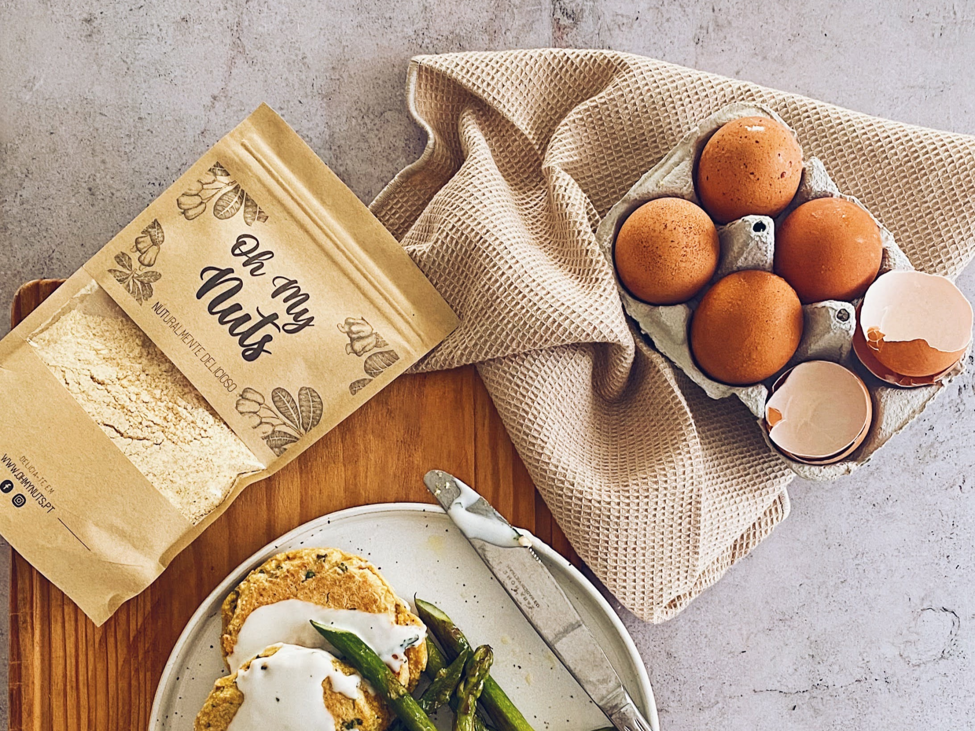 Pacote de farinha, ovos castanhos, prato com comida e guardanapo sobre mesa cinza