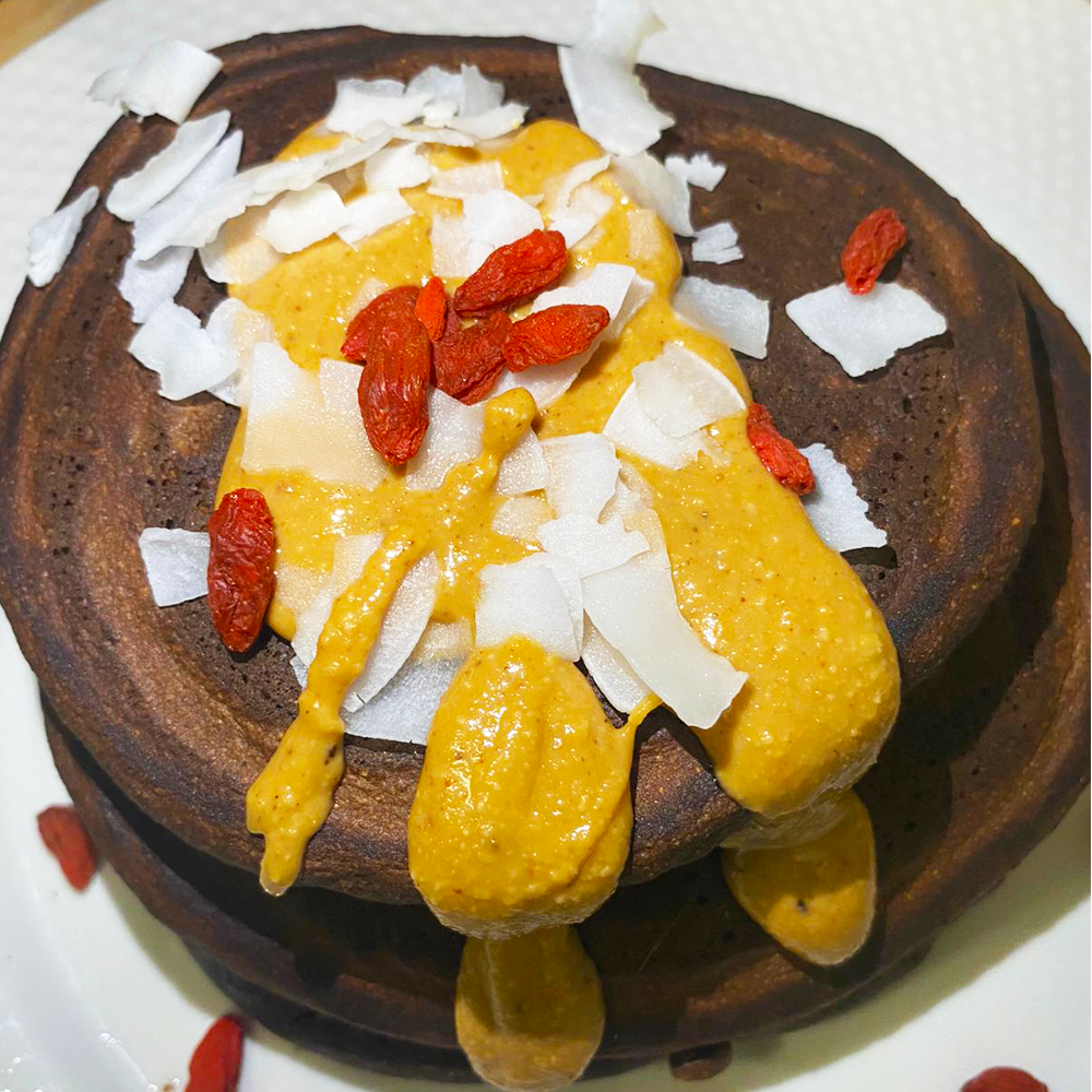 Bolo escuro com cobertura amarela, flocos brancos e bagas vermelhas num prato branco