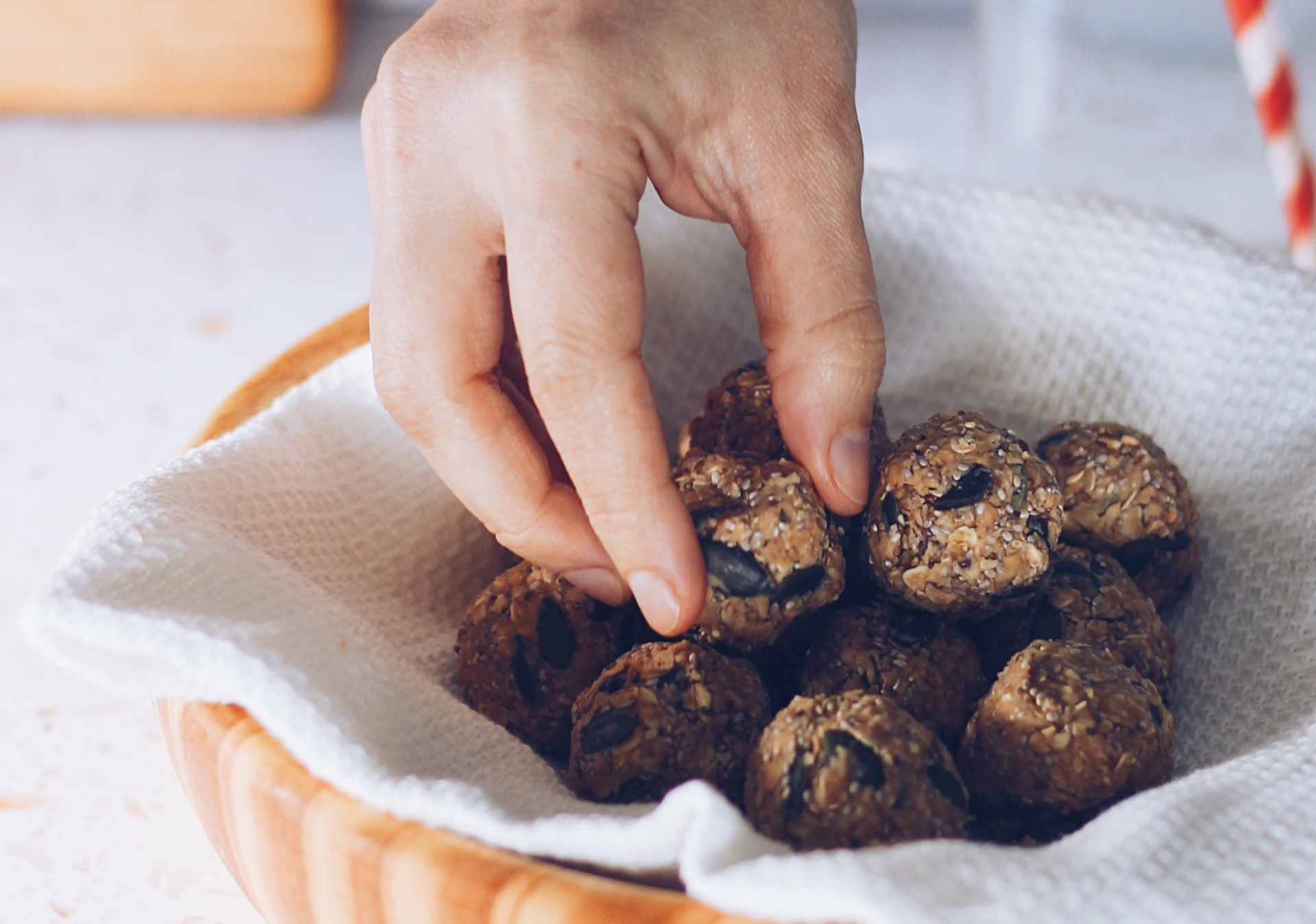 Bolinha de aveia e frutos secos numa tigela de madeira forrada com pano branco, mão a pegar numa bolinha.