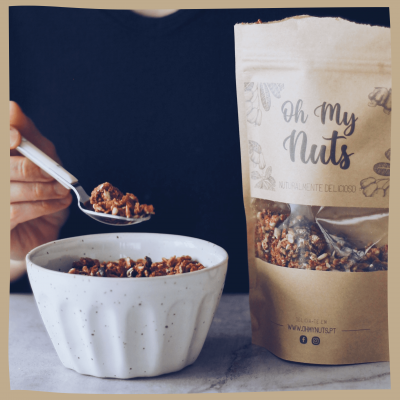 Pacote de granola Oh My Nuts ao lado de tigela branca com granola e colher