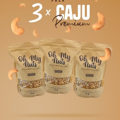 Três embalagens de caju premium Oh My Nuts 500g em fundo bege com cajus flutuantes