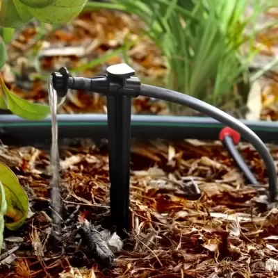 aspersor preto a jorrar água no jardim com plantas verdes e solo com cobertura de casca