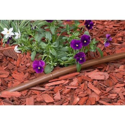 Aspersor de irrigação castanho na terra coberta de casca de pinheiro vermelha junto a flores roxas e brancas.