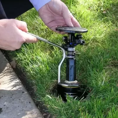 Sistema de aspersão de relva preto com partes metálicas junto a passeio