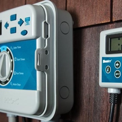 Painel de controlo de rega eletrónico Hunter e controlador SOIL-CLIK numa parede de madeira.