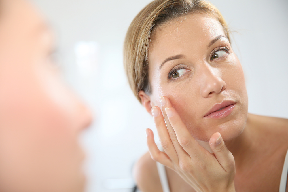 Mulher a aplicar creme facial no espelho