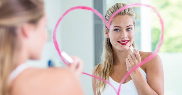 Mulher aplica batom refletida num espelho com um coração desenhado