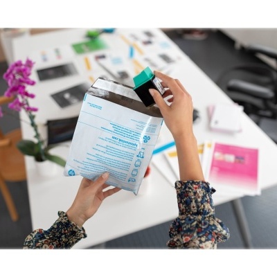 Mãos segurando saco branco e azul com texto em ambiente de escritório moderno