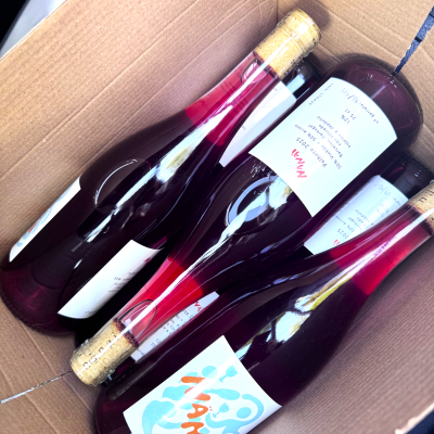 Garrafas de vinho em caixa de cartão com etiquetas brancas e texto em português.