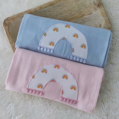 Toalhas azul e rosa com aplicação de arco-íris e pompons em fundo branco felpudo