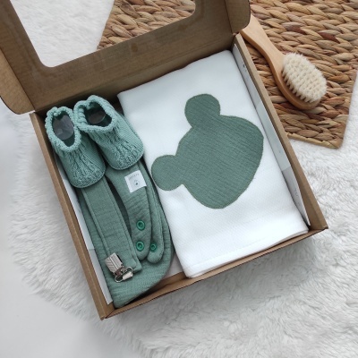 Conjunto de bebé com sapatinhos, suspensórios e manta com rosto de urso em caixa de cartão aberta